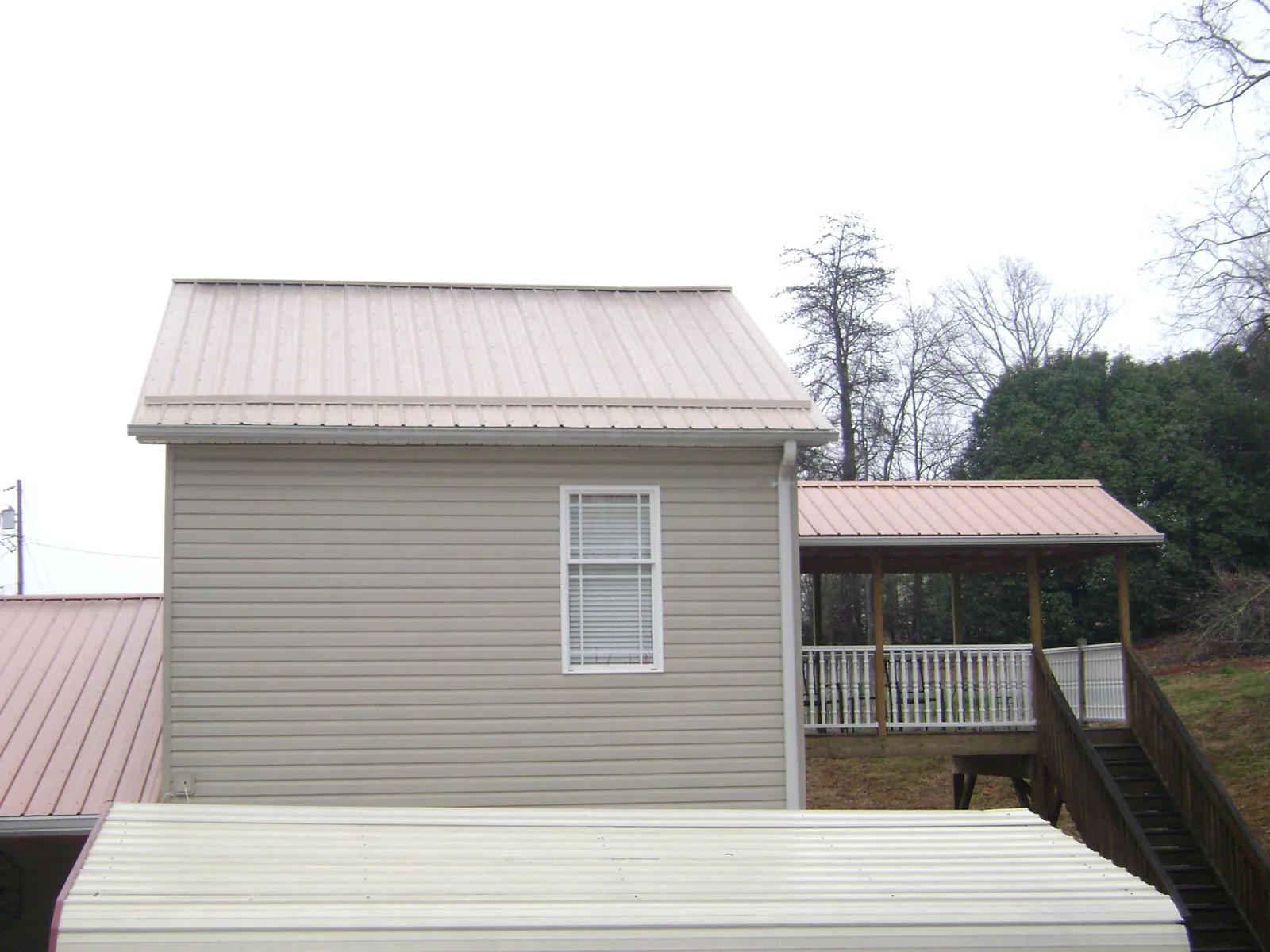 Tan metal roofs on a two story addition and attached porch, from a Roof Replacement job in Olivia